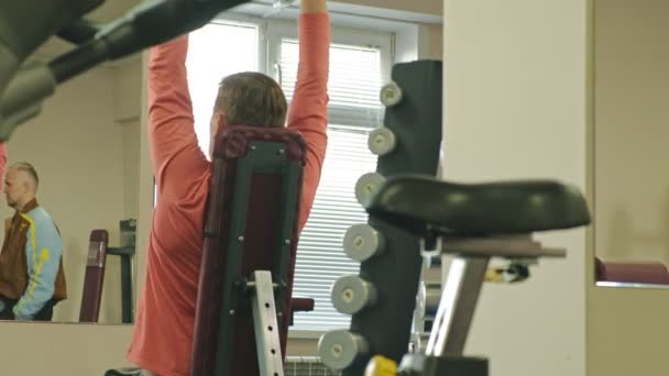 Een man doet een bankdrukken met dumbbells zittend met een rechte greep in een fitness studio — Stockvideo