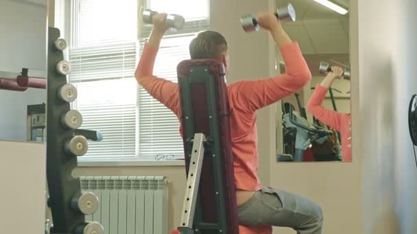 Een man doet een bankdrukken met dumbbells zittend met een rechte greep in een fitness studio — Stockvideo