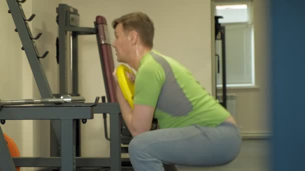 De overgewicht man doet squats met squats met een gewicht schijf voor een barbell. Fitness training. Gezond lifestyle concept — Stockvideo