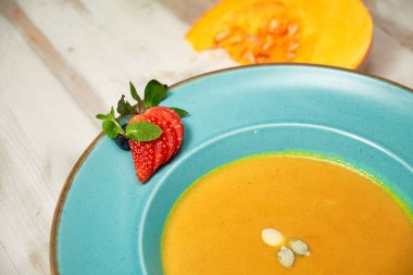 Kabak çekirdeği ile mavi bir tabakta kabak çorbası püresi. Açık ahşap arka plan.