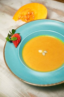 Kabak çekirdeği ile mavi bir tabakta kabak çorbası püresi. Açık ahşap arka plan.
