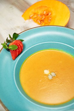 Kabak çekirdeği ile mavi bir tabakta kabak çorbası püresi. Açık ahşap arka plan.