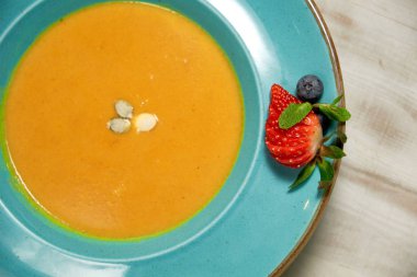 Kabak çekirdeği ile mavi bir tabakta kabak çorbası püresi. Açık ahşap arka plan.