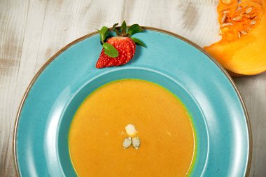 Kabak çekirdeği ile mavi bir tabakta kabak çorbası püresi. Açık ahşap arka plan.