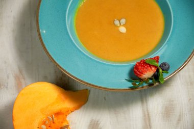 Kabak çekirdeği ile mavi bir tabakta kabak çorbası püresi. Açık ahşap arka plan.