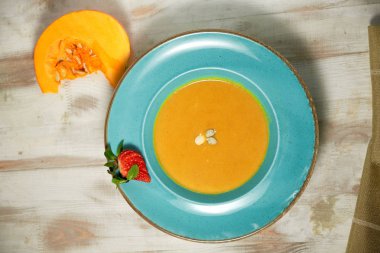 Kabak çekirdeği ile mavi bir tabakta kabak çorbası püresi. Açık ahşap arka plan.