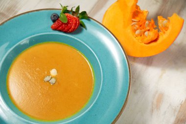 Kabak çekirdeği ile mavi bir tabakta kabak çorbası püresi. Açık ahşap arka plan.