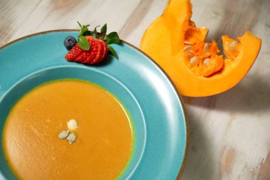 Kabak çekirdeği ile mavi bir tabakta kabak çorbası püresi. Açık ahşap arka plan.