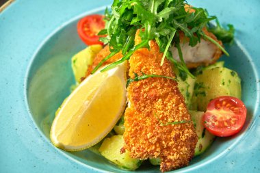 Mavi tabakta sebze ve otlar ile Ekmekli tavuk. Koyu ahşap arka plan. Restoran yemekleri.