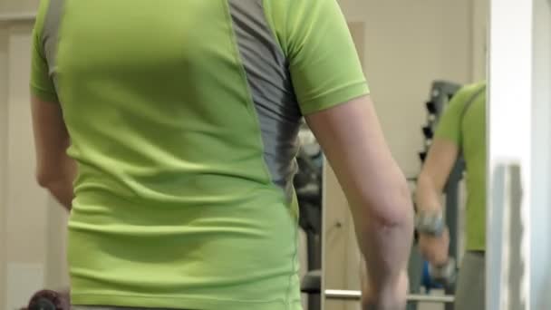 A overweight man lifts an ez barbell while standing at the gym. Exercise for biceps. Fitness. Healthy lifestyle. — Stock Video