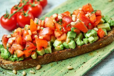 Domates ve avokado ile brusket yeşil bir tabak üzerinde. Açık gri dokulu arka plan. Yemeklerin güzel bir porsiyon. Restoran menüsü