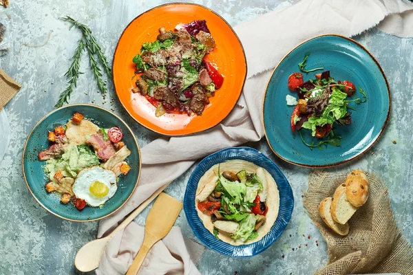 Farklı salatalar ile çok renkli tabaklar. Yemeklerin güzel bir porsiyon. Açık gri arka plan. Restoran menüsü