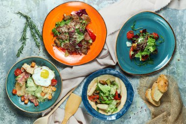Farklı salatalar ile çok renkli tabaklar. Yemeklerin güzel bir porsiyon. Açık gri arka plan. Restoran menüsü