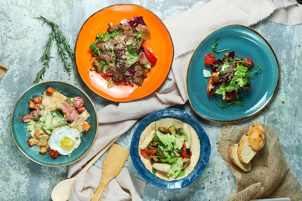 Farklı salatalar ile çok renkli tabaklar. Yemeklerin güzel bir porsiyon. Açık gri arka plan. Restoran menüsü