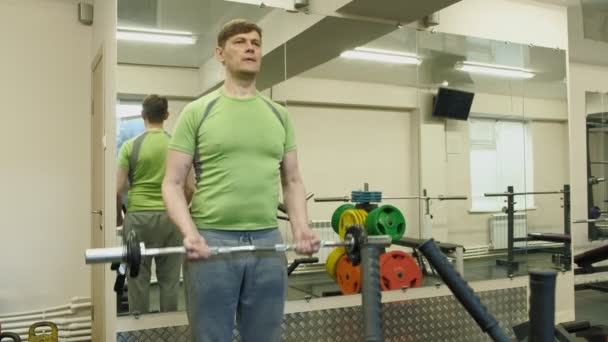 Un hombre con sobrepeso levanta una barra de ez mientras está parado en el gimnasio. Ejercicio para bíceps. Fitness. Estilo de vida saludable . — Vídeo de stock