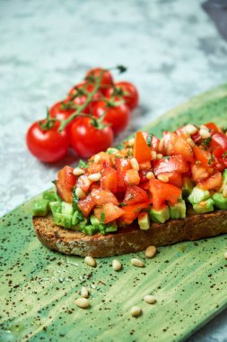 Domates ve avokado ile brusket yeşil bir tabak üzerinde. Açık gri dokulu arka plan. Yemeklerin güzel bir porsiyon. Restoran menüsü