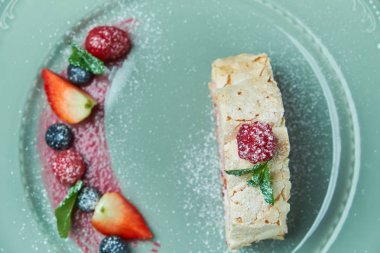 Böğürtlenli bir tabakta, gri bir arka plan üzerinde beze kek rulo dilim