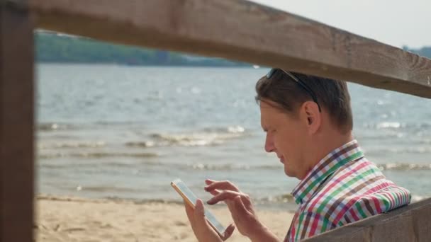 Un uomo sulla spiaggia usa un tablet per computer . — Video Stock