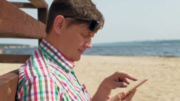 Ein Mann am Strand benutzt ein Computer-Tablet. — Stockvideo