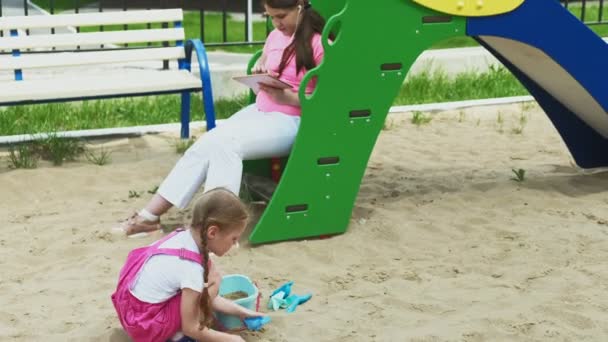 Children use a computer tablet, walk on the playground — Stock Video