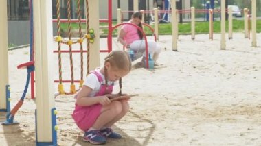 Çocuklar bilgisayar tableti kullanır, oyun alanında yürürler.