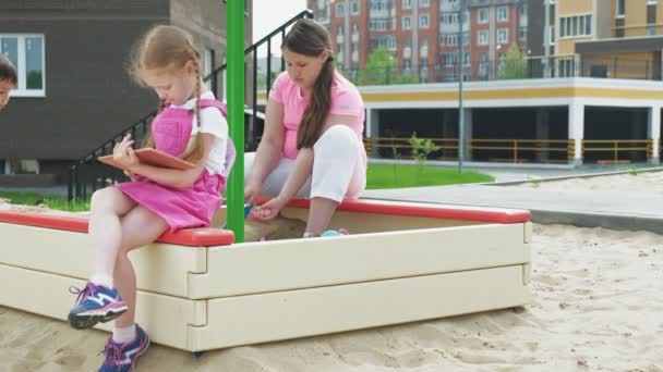 Children use a computer tablet, walk on the playground — Stock Video