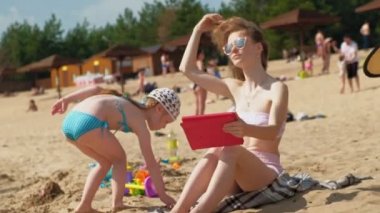 Genç bir kadın sahilde, nehir kıyısında bilgisayar tableti kullanıyor.