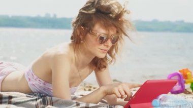 Genç bir kadın sahilde, nehir kıyısında bilgisayar tableti kullanıyor.