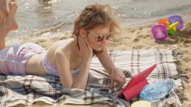 Genç bir kadın sahilde, nehir kıyısında bilgisayar tableti kullanıyor.