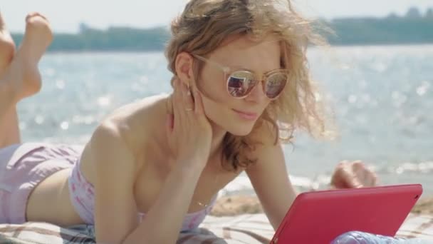 Giovane donna utilizza tablet computer sulla spiaggia, riva del fiume — Video Stock