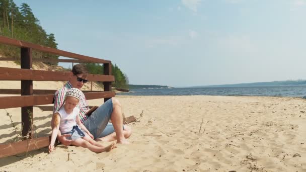 Papá y su hija están usando una tableta al aire libre. Ribera del río — Vídeos de Stock