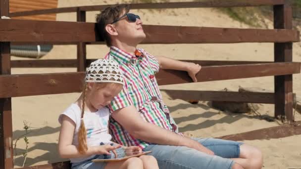 Papá y su hija están usando una tableta al aire libre. Ribera del río — Vídeos de Stock
