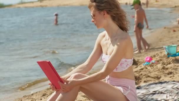 Mujer joven utiliza tableta de ordenador en la playa, orilla del río — Vídeo de stock