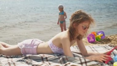 Genç bir kadın sahilde, nehir kıyısında bilgisayar tableti kullanıyor.