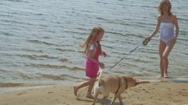 Anne ve kızı bir köpekle nehir kıyısında koşarlar. Güneşli bir yaz günü. Aile tatili