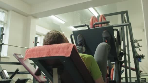 Ein Mann mit Übergewicht macht Beinpressen auf dem Simulator in der Sporthalle. Fitnesstraining. Konzept eines gesunden Lebensstils — Stockvideo