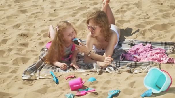 Mãe e filha na margem do rio comem sorvete. Recreação ao ar livre — Vídeo de Stock