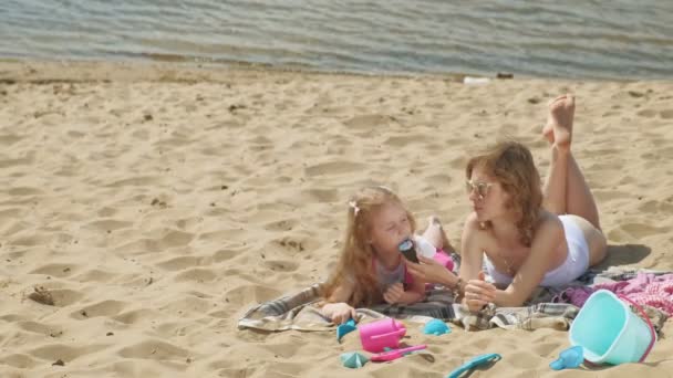Mamá e hija en la orilla del río comen helado. recreación al aire libre — Vídeo de stock