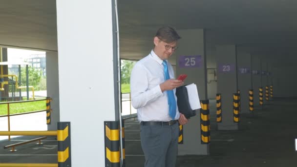 商人在空车场的背景下使用手机. — 图库视频影像