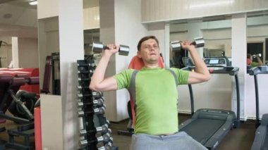 Bir adam bir fitness stüdyosunda düz bir kavrama ile oturan dumbbells ile bir bank basın yapıyor