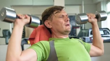 Bir adam bir fitness stüdyosunda düz bir kavrama ile oturan dumbbells ile bir bank basın yapıyor