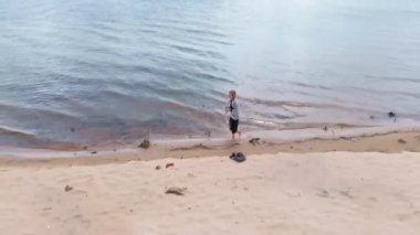 Elbiseli genç bir kadın sahil boyunca koşuyor. Hava çekimi