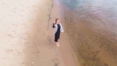 Elbiseli genç bir kadın sahil boyunca koşuyor. Hava çekimi