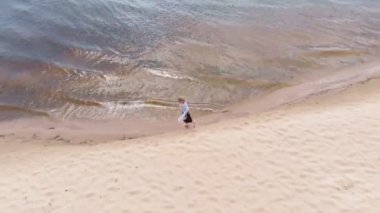 Elbiseli genç bir kadın sahil boyunca koşuyor. Hava çekimi