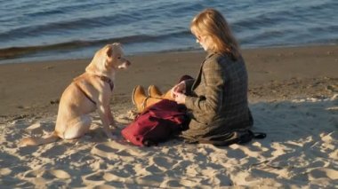 Nehir kıyısındaki sahilde genç bir kadın, lobrodor diye kahverengi bir köpeği besliyor. İlkbahar veya soğuk yaz