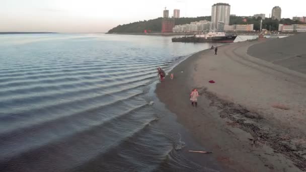 Mãe e filha, corram, brinquem com um labrador de cães castanhos na praia junto ao rio. Filmagem aérea — Vídeo de Stock