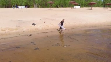 Elbiseli genç bir kadın sahil boyunca koşuyor. Hava çekimi