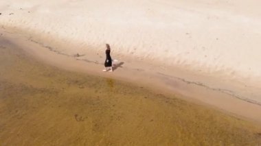 Elbiseli genç bir kadın sahil boyunca koşuyor. Hava çekimi