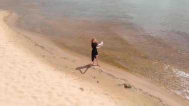 Elbiseli genç bir kadın sahil boyunca koşuyor. Hava çekimi