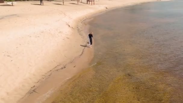 Una joven con un vestido corre por la playa. Disparo aéreo — Vídeos de Stock